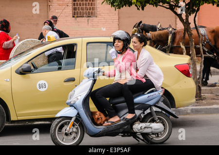 Zwei junge Frauen, die Fahrt entlang einer Straße in einem Motorroller, Marrakesch, Marokko Stockfoto