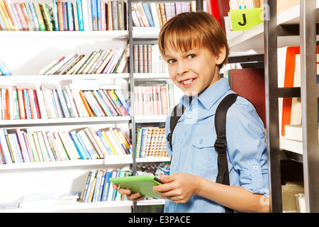 Süsser Boy steht und hält Bücher in der Bibliothek Stockfoto