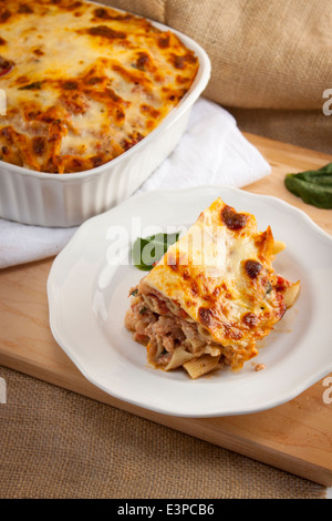 Italienische baked ziti auf Platte mit vollen Kasserolle im Hintergrund dienen. Gabel mit Biss. Sieht aus wie Lasagne Stockfoto