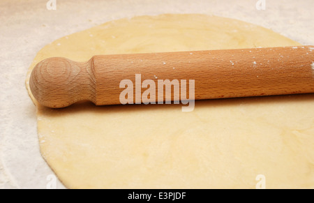 Frisches Gebäck auf einer bemehlten Arbeitsfläche mit einem hölzernen Nudelholz ausgerollt Stockfoto