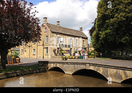 Stein-Fußgängerbrücke über den Fluss Windrush mit Kingsbridge Inn nach hinten, Bourton auf dem Wasser, England, UK. Stockfoto
