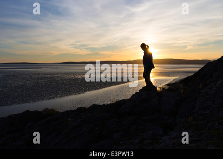 Frau zu Fuß entlang der Küste Silverdale bei Sonnenuntergang, Morecambe Bay, Lancashire, England UK Stockfoto