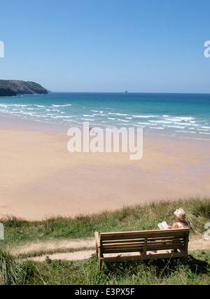 Frau setzte sich auf eine öffentliche Bank und liest ein Buch mit Blick auf Perranporth Strand, Cornwall, UK Stockfoto