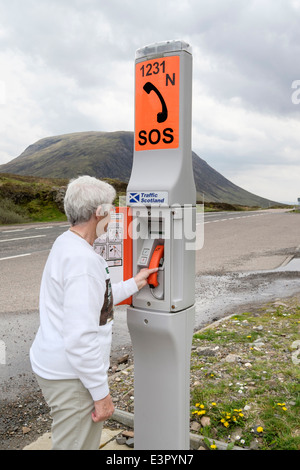 Ältere Frau mit einer SOS-Notruf neben einer abgelegenen Landstraße. Glen Coe, Highland, Schottland, Großbritannien Stockfoto