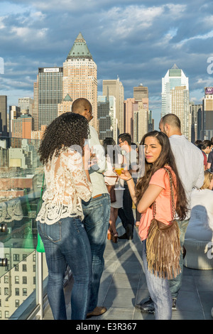 Junge Paare gemischtrassigen Gruppe drängen Geländer Ink48 Hotel Rooftop Bar Presselounge genießen Blick auf den Sonnenuntergang von Midtown Manhattan Skyline von New York City Stockfoto