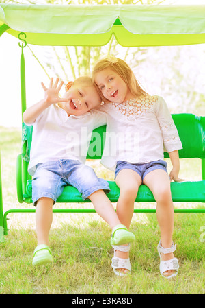 Niedlichen kleinen Bruder und Schwester, die Spaß auf der Schaukel im Hinterhof, fröhliche Kinder in Kindertagesstätten, Liebe und Freundschaft-Konzept Stockfoto