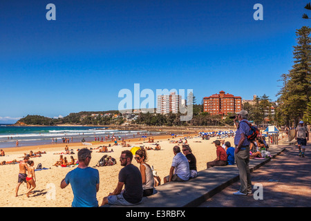 Manly Beach, Sydney, Australien. Ältere Menschen nehmen Foto mit seinem Handy. Schlange von Menschen, die auf einer Mauer sitzend. Stockfoto