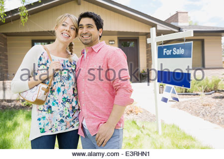 Paar lächelnd neben For Sale Schild