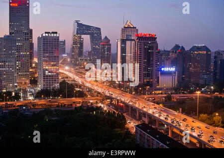 Schöner Blick auf die Skyline von Jianwai Soho und das berühmte Wahrzeichen des CCTV-Hauptquartiers, mit den Lichtern des Verkehrs auf der dritten Ringstraße und Büros und Gebäuden, die die Szene am frühen Abend erhellen. Seltene Panorama-Szene während der blauen Stunde kurz nach Sonnenuntergang mit klarem Himmel in Guomao, dem zentralen Geschäftsviertel der chinesischen Hauptstadt Peking, befindet sich im Chaoyang Bezirk, China, PRC. © Olli Geibel Stockfoto