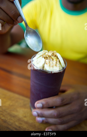 Brasilianischen Mann in Brasilien Farben Shirt Verzehr einer Tasse frisch gefrorene Acai Açaí mit Banane Stockfoto