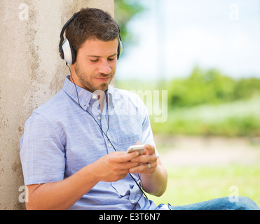 Junger Mann mit Handy und Kopfhörer außerhalb Stockfoto
