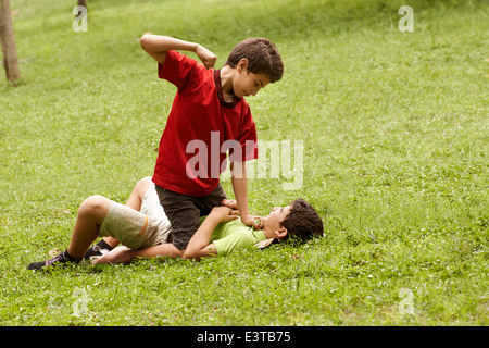 Zwei junge Brüder kämpfen und schlagen auf dem Rasen im Park, mit älteren Jungen sitzen über der jüngere Stockfoto