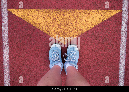 Ein Läufer steht mit ihren Schuhen zeigte auf ein gelbes Dreieck auf einer roten Laufstrecke. Stockfoto
