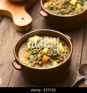 Vegetarische Suppe aus Linsen, Spinat, Kartoffeln, Karotten und Zwiebel in dunklen braunen Schalen serviert Stockfoto