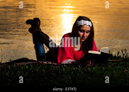 Eine hübsche junge Dame ein Buch an den Ufern des Kentucky Lake zu lesen, als die Sonne aufgeht. Stockfoto