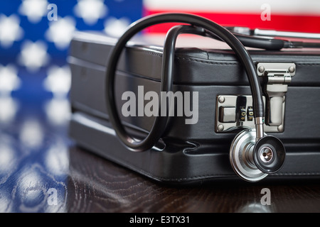 Aktentasche aus Leder und Stethoskop ruhen auf Tisch mit amerikanischen Flagge hinter. Stockfoto