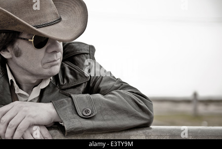 Porträt eines nachdenklich, modernen Tag Cowboy, Zaun gelehnt. Farben entfernt, aber nicht ganz schwarz & weiß. Stockfoto