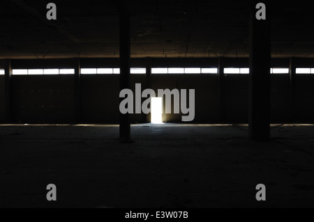 Dunklen Innenraum in verlassenen Fabrik Betonsäulen und Licht durch die Ausgangstür. Industrieruine. Stockfoto