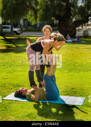 Ein Trio von Athleten führen Acroyoga in Balboa Park, San Diego, CA. beachten Sie die Basis auf dem Boden, der Flyer statt den Boden und der Spotter, die beiden anderen Kritiken. Die Aktivität verbindet Elemente aus Yoga, Akrobatik, Performance und Heilkunst. Stockfoto