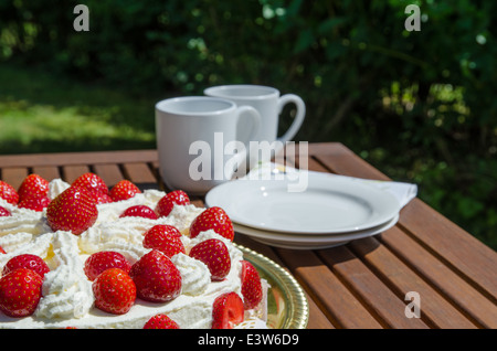 Tisch im Freien im Garten mit Erdbeerkuchen und Kaffeetassen im Hintergrund Stockfoto