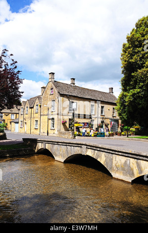 Stein-Fußgängerbrücke über den Fluss Windrush mit Kingsbridge Inn nach hinten, Bourton auf dem Wasser, England, UK. Stockfoto