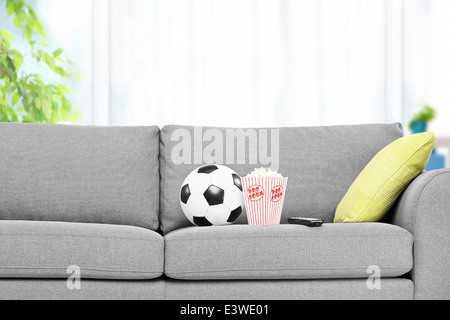 Fußball und eine Schachtel mit Popcorn auf ein modernes Sofa, drinnen Stockfoto