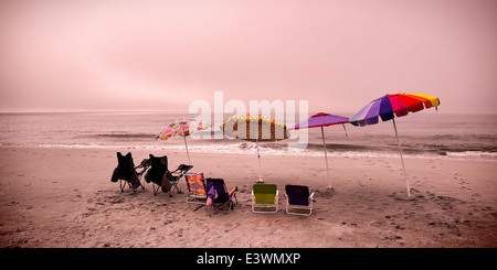 Leer und düsteren Strand-Szene mit frei gewordenen Liegestühle und Sonnenschirme Stockfoto