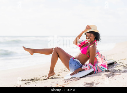 Afroamerikanische Frau sitzt auf Surfbrett am Strand Stockfoto