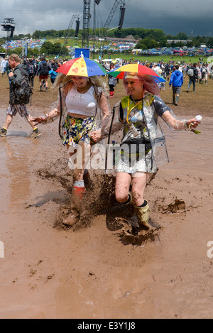 Pilton, UK, 27.06.2014: Atmosphäre beim Glastonbury Festival. Zwei junge Frauen durchlaufen einer großen schlammige Pfütze. Bild von Julie Edwards Stockfoto