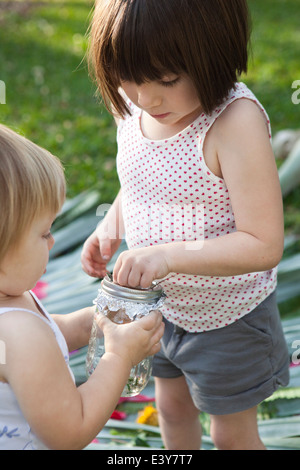 Mädchen und Kleinkind Schwester hält Glas mit grünen Anole Eidechse im Garten Stockfoto