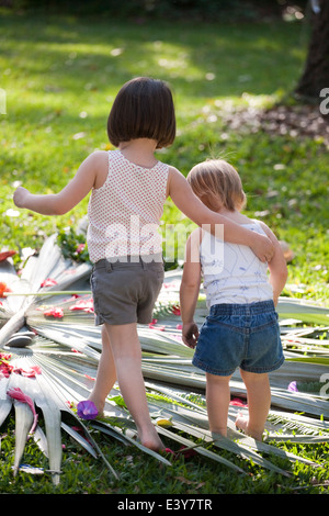 Mädchen mit Arm um Kleinkind Schwester mit Blume und Blatt-Anzeige im Garten Stockfoto