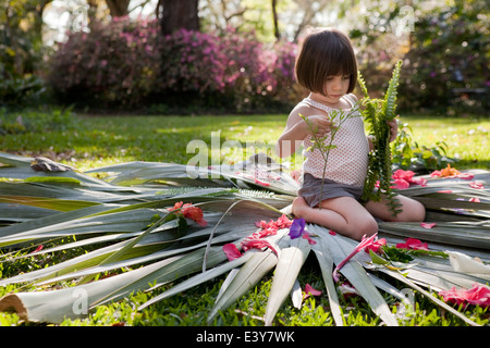 Mädchen mit Farn Blume und Blatt Display im Garten sitzen Stockfoto