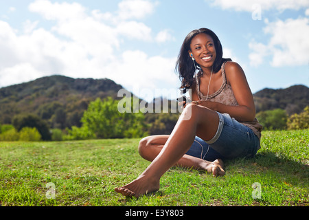 Junge Frau sitzt auf grasbewachsenen Hügel Stockfoto