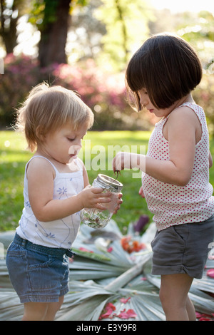 Mädchen und Kleinkind Schwester mit grünen Anole Eidechse und Glas im Garten Stockfoto