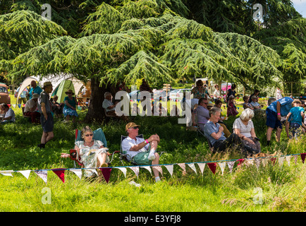 East Devon, England. Leute sitzen, entspannen im Schatten eines großen Baumes auf einer Fete und Gartenfest im Sommer. Stockfoto