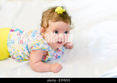 Ein drei Monate altes Kaukasischen kleinkind Mädchen liegt auf dem Bauch und lächelt. Gelbe Kleidung und weiße Decke. Nahaufnahme. Stockfoto