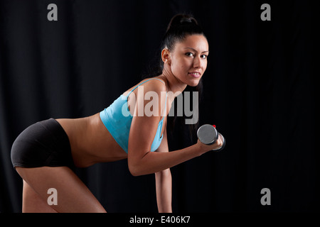 Frau mit einem perfekten Körper, Gewichte zu heben und auf schwarzem Hintergrund isoliert Stockfoto