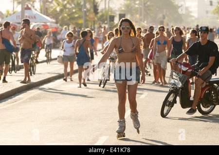 RIO DE JANEIRO, Brasilien - 19. Januar 2014: Brasilianische Mann auf e-Bike folgt Frau auf Inline-Skates und Massen in Ipanema Stockfoto