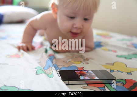 Baby spielt mit Smartphone auf Bett Stockfoto