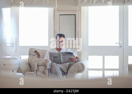 Reifer Mann liest Zeitung im Wohnzimmer Stockfoto