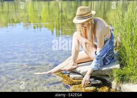 Junge Frau sitzt auf den Felsen von Wasser Stockfoto