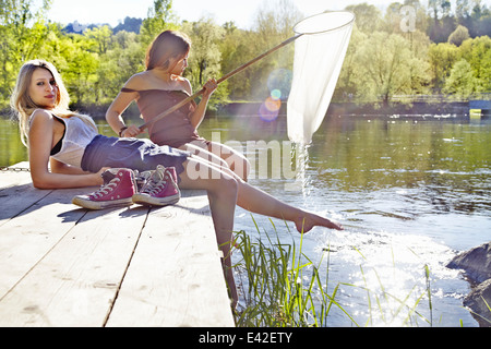 Junge Frauen sitzen auf Steg, eine Holding Fischernetz Stockfoto