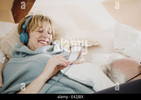 Reife Frau auf Bett mit MP3-player Stockfoto