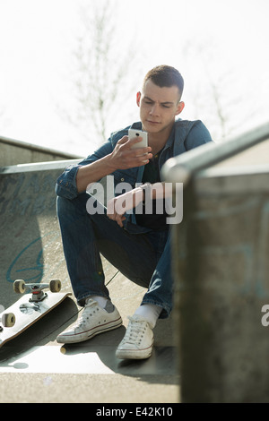 Skateboarder auf Rampe, sitzen mit smartphone Stockfoto