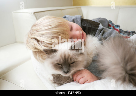 Niedlichen drei Jahre alten Jungen mit Augen geschlossen umarmt Katze auf sofa Stockfoto