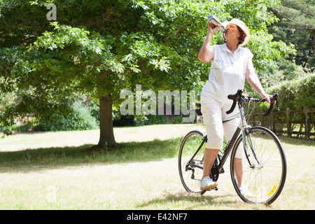 Ältere Frau Radfahrer Trinkwasser im park Stockfoto