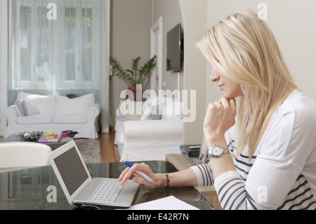 Junge Frau, die Eingabe auf Laptop zu Hause Schreibtisch Stockfoto