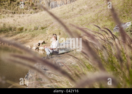 Junge Frau in Yogaposition am Seeufer Stockfoto