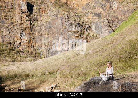 Junge Frau in Yogaposition auf Felsen am See Stockfoto