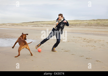 Mitte erwachsenen Mann mit Hund spielen Fußball am Strand, Bloemendaal Aan Zee, Niederlande Stockfoto